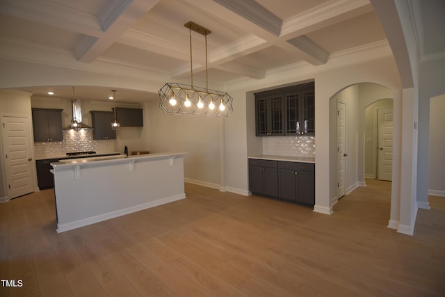 kitchen featuring wall chimney range hood, beam ceiling, arched walkways, and wood finished floors