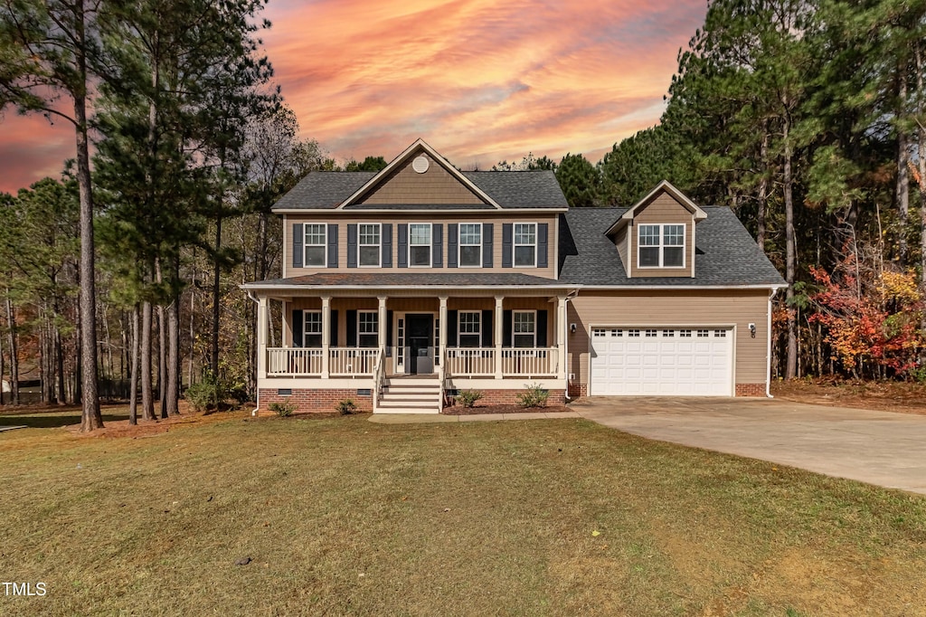 colonial home with covered porch, a garage, and a lawn