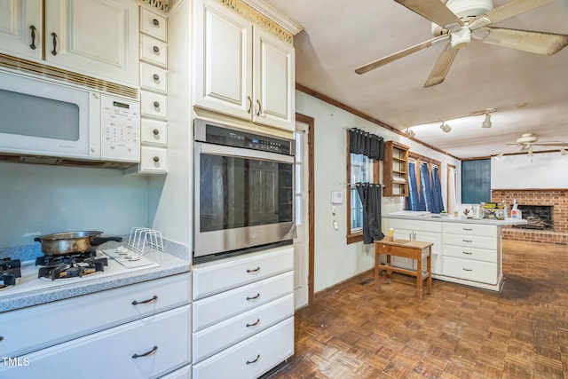 kitchen with a brick fireplace, dark parquet floors, white appliances, ceiling fan, and crown molding