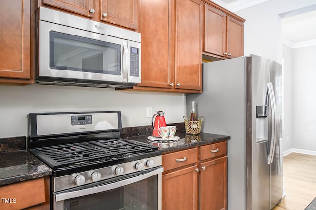 kitchen with stainless steel appliances, light hardwood / wood-style floors, crown molding, and dark stone countertops