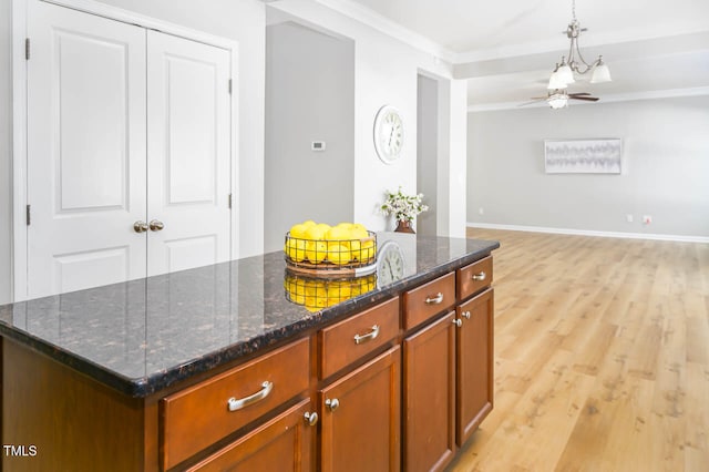 kitchen with ornamental molding, dark stone counters, ceiling fan, light hardwood / wood-style flooring, and a kitchen island