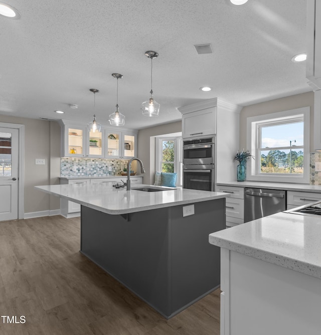 kitchen featuring sink, hanging light fixtures, stainless steel appliances, an island with sink, and white cabinets