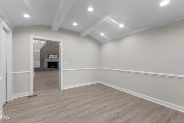 empty room featuring a fireplace, lofted ceiling with beams, and light wood-type flooring