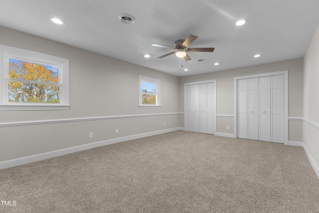 unfurnished bedroom with two closets, a textured ceiling, ceiling fan, and carpet flooring