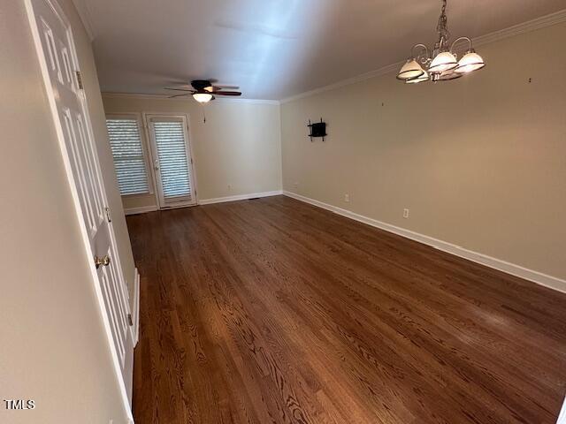 empty room with ceiling fan with notable chandelier, dark hardwood / wood-style flooring, and ornamental molding