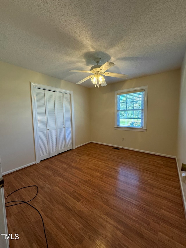 unfurnished bedroom with ceiling fan, wood-type flooring, a textured ceiling, and a closet