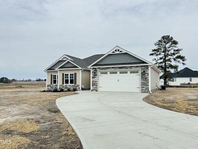 craftsman-style house featuring concrete driveway, an attached garage, central AC unit, and stone siding