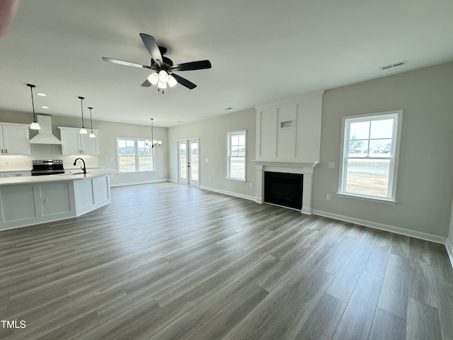 unfurnished living room with visible vents, a sink, wood finished floors, a fireplace, and baseboards