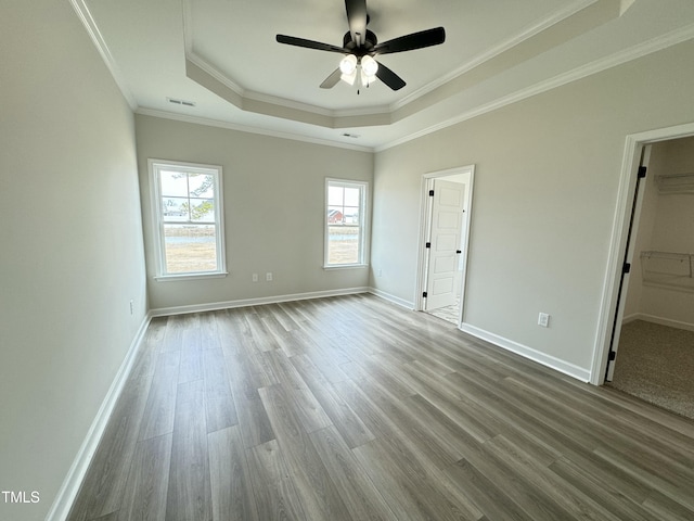 unfurnished bedroom featuring visible vents, a raised ceiling, ornamental molding, wood finished floors, and baseboards