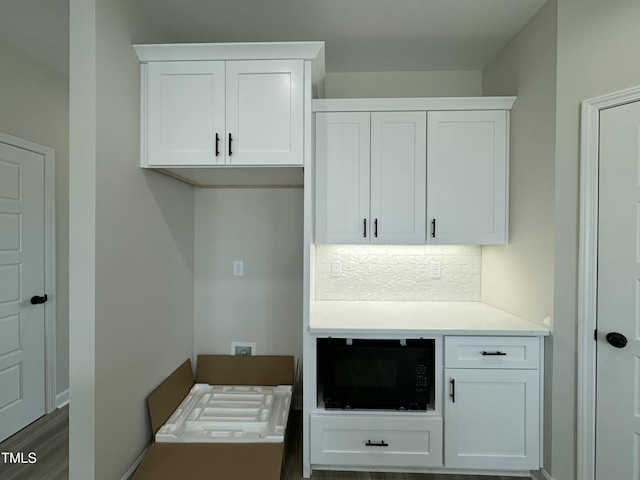 kitchen with decorative backsplash, light countertops, white cabinets, and black microwave