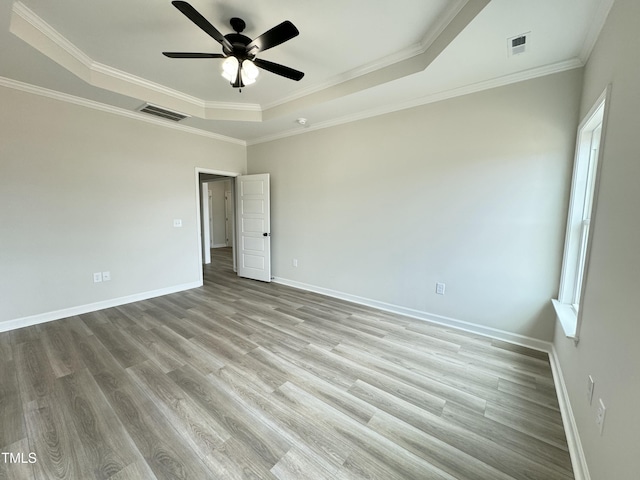 unfurnished bedroom featuring visible vents, baseboards, a tray ceiling, and wood finished floors