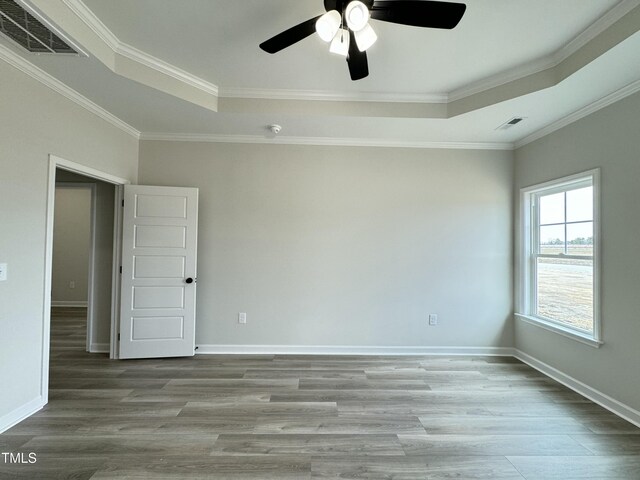 empty room featuring visible vents, a raised ceiling, baseboards, and wood finished floors