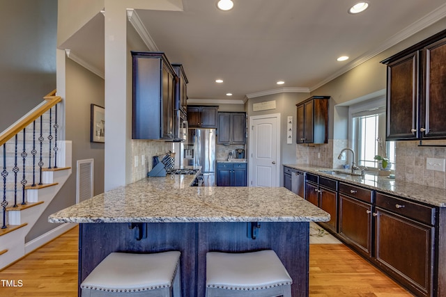 kitchen with light hardwood / wood-style floors, a breakfast bar area, ornamental molding, and sink