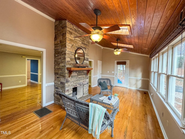 living room featuring vaulted ceiling with skylight, wood ceiling, light wood-type flooring, ornamental molding, and a fireplace