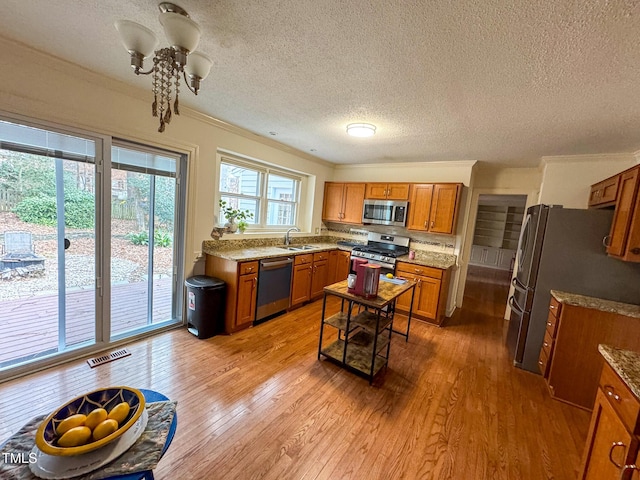 kitchen featuring appliances with stainless steel finishes, sink, light hardwood / wood-style floors, crown molding, and a textured ceiling