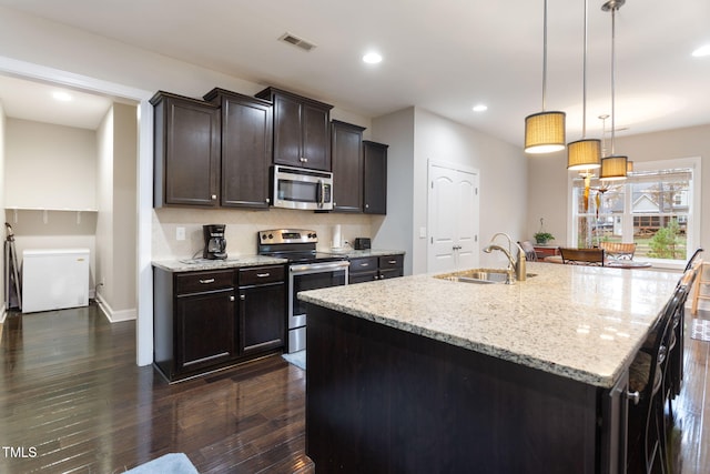 kitchen featuring sink, dark brown cabinets, hanging light fixtures, stainless steel appliances, and a kitchen island with sink