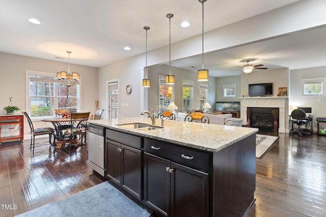 kitchen with pendant lighting, an island with sink, sink, stainless steel dishwasher, and light stone countertops