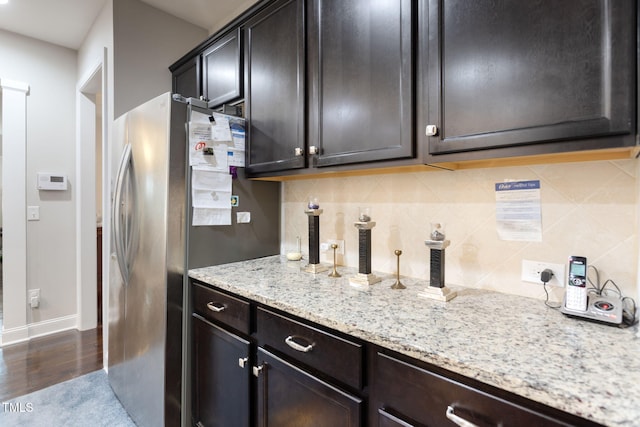 kitchen with dark brown cabinetry, dark hardwood / wood-style flooring, stainless steel fridge, light stone countertops, and decorative backsplash