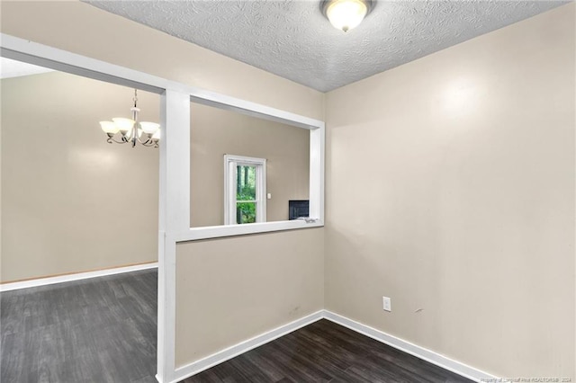 spare room featuring a textured ceiling, dark wood-type flooring, and a notable chandelier