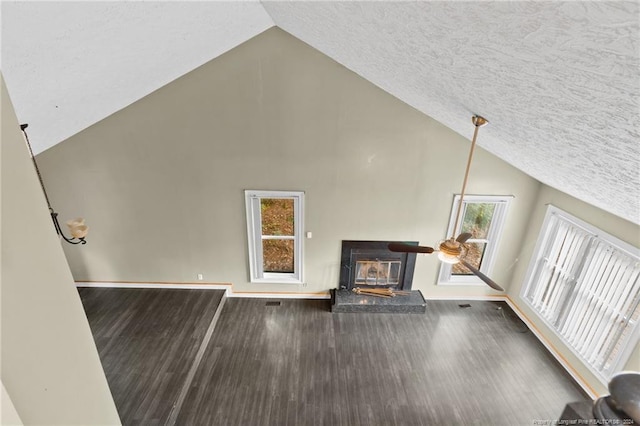 unfurnished living room featuring wood-type flooring, high vaulted ceiling, plenty of natural light, and a wood stove