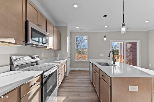 kitchen with appliances with stainless steel finishes, ornamental molding, sink, a center island with sink, and decorative light fixtures