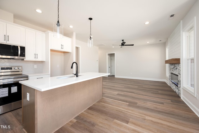 kitchen with a stone fireplace, a sink, visible vents, light wood-style floors, and appliances with stainless steel finishes