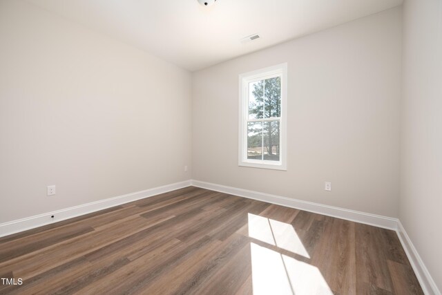 spare room featuring dark wood-style floors, visible vents, and baseboards