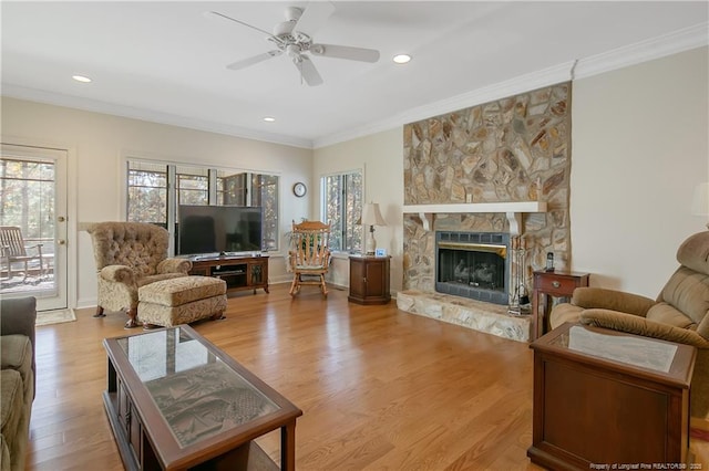 living room with ceiling fan, a stone fireplace, light wood-type flooring, and crown molding