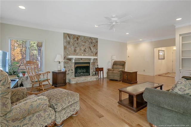 living room with light hardwood / wood-style flooring, a stone fireplace, ceiling fan, and ornamental molding