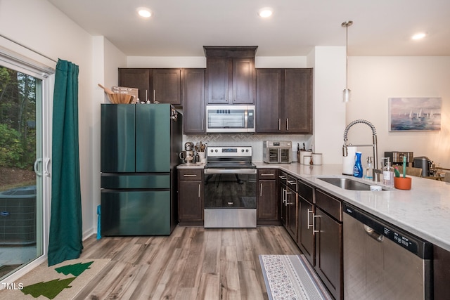 kitchen featuring sink, light hardwood / wood-style flooring, pendant lighting, decorative backsplash, and appliances with stainless steel finishes