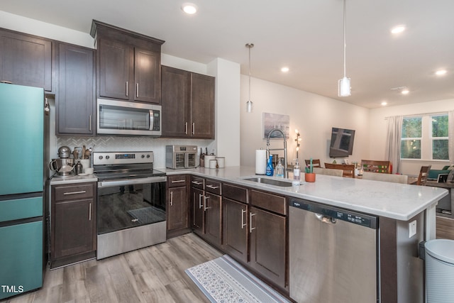 kitchen featuring sink, stainless steel appliances, light hardwood / wood-style flooring, kitchen peninsula, and pendant lighting