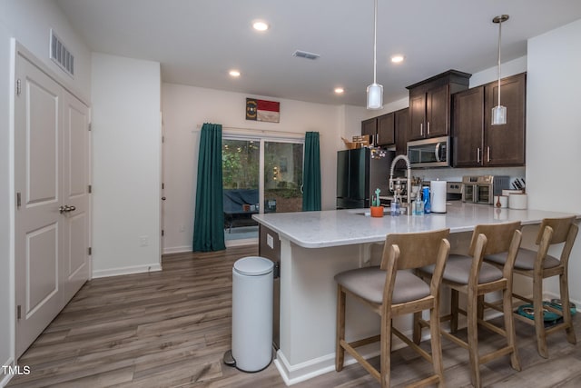 kitchen with pendant lighting, black fridge, dark brown cabinets, light hardwood / wood-style floors, and a kitchen bar