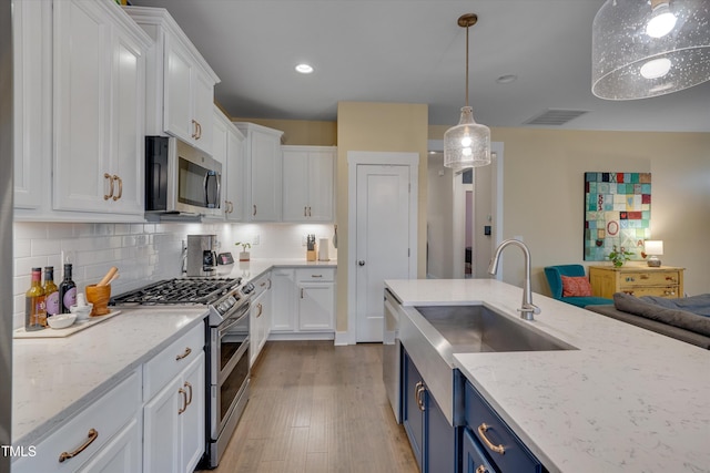 kitchen with stainless steel appliances, white cabinetry, light stone countertops, and blue cabinetry