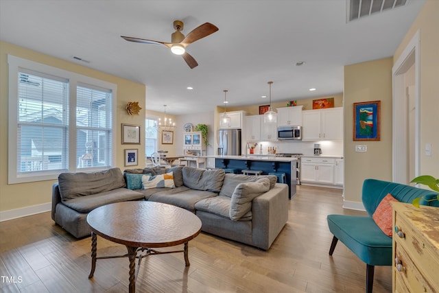 living room with ceiling fan with notable chandelier and light hardwood / wood-style floors