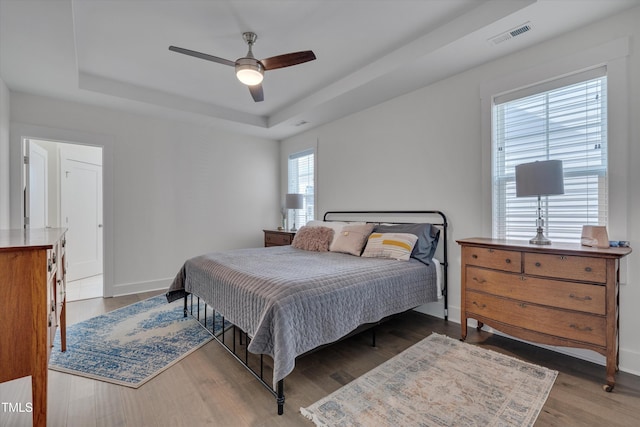 bedroom with wood-type flooring, ceiling fan, and a tray ceiling