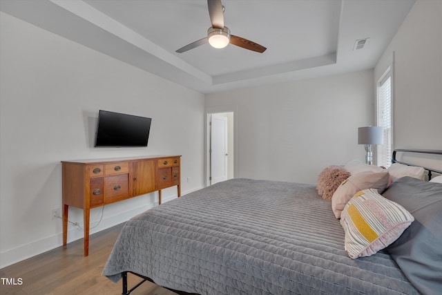 bedroom with ceiling fan, wood-type flooring, and a tray ceiling