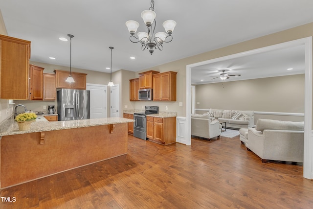 kitchen with sink, hardwood / wood-style flooring, light stone countertops, appliances with stainless steel finishes, and a breakfast bar area