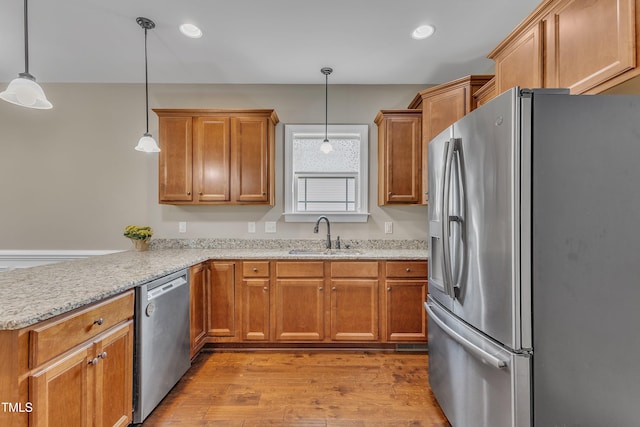 kitchen featuring kitchen peninsula, stainless steel appliances, sink, light hardwood / wood-style flooring, and hanging light fixtures