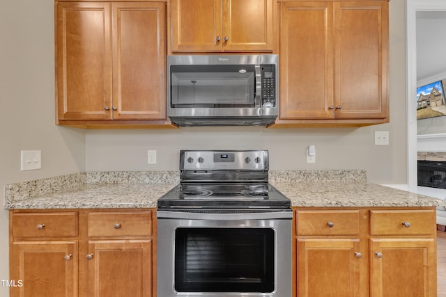 kitchen with a stone fireplace, light stone counters, and stainless steel appliances