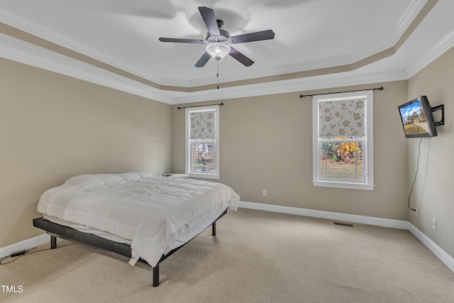 carpeted bedroom featuring a tray ceiling, multiple windows, ceiling fan, and crown molding