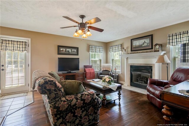 living room featuring a textured ceiling, ceiling fan, dark wood-type flooring, and a tiled fireplace