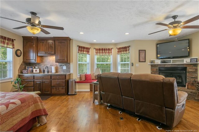 bedroom with a textured ceiling, ceiling fan, light wood-type flooring, and a fireplace