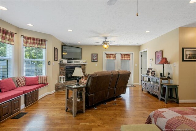 living room featuring a textured ceiling, ceiling fan, light hardwood / wood-style floors, and a fireplace