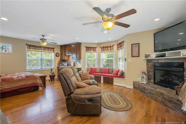 living area featuring a fireplace, a ceiling fan, light wood finished floors, and baseboards
