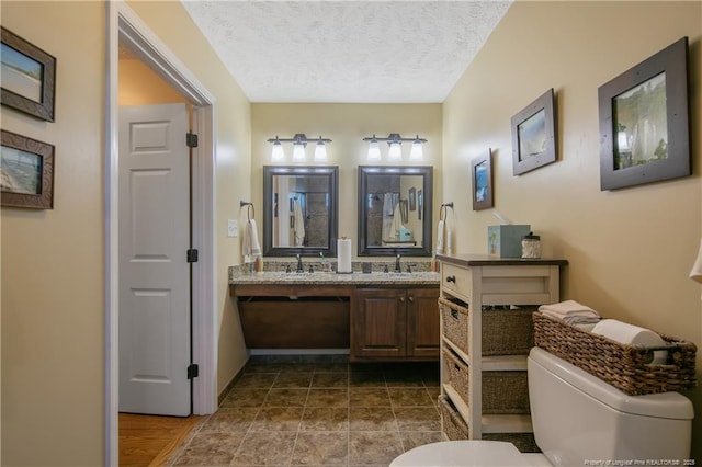 full bathroom featuring toilet, a textured ceiling, a sink, and double vanity