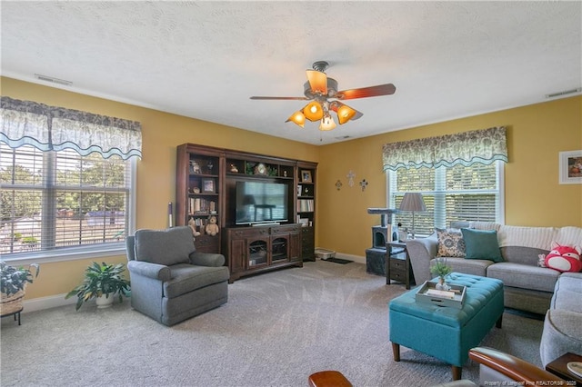 carpeted living area featuring a textured ceiling, visible vents, ceiling fan, and baseboards