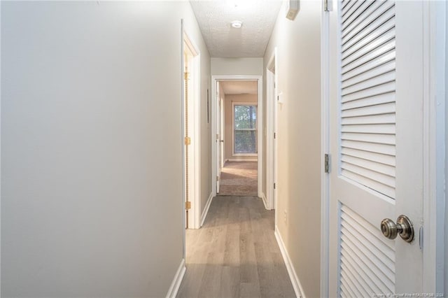 corridor with a textured ceiling and light hardwood / wood-style floors