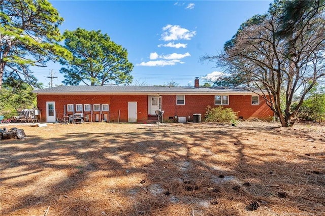 back of house with entry steps, a chimney, central AC, and brick siding