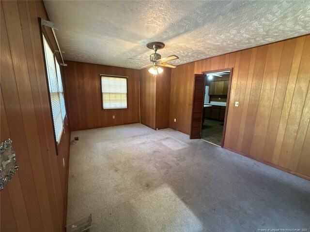 unfurnished room with ceiling fan, wood walls, and light carpet