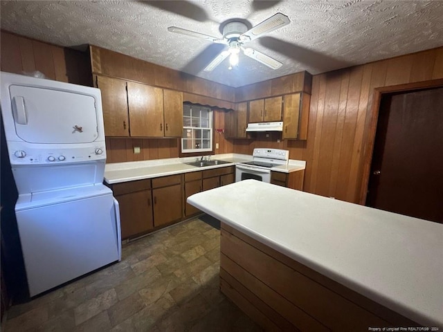 kitchen featuring stacked washer and clothes dryer, electric stove, sink, wooden walls, and a textured ceiling